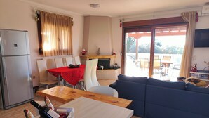 A compact living space with a dining area, a sofa, a kitchen with a refrigerator, and a balcony with a table and chairs. - Villa Traditional Estate Heated Pool (Nea Propontida)