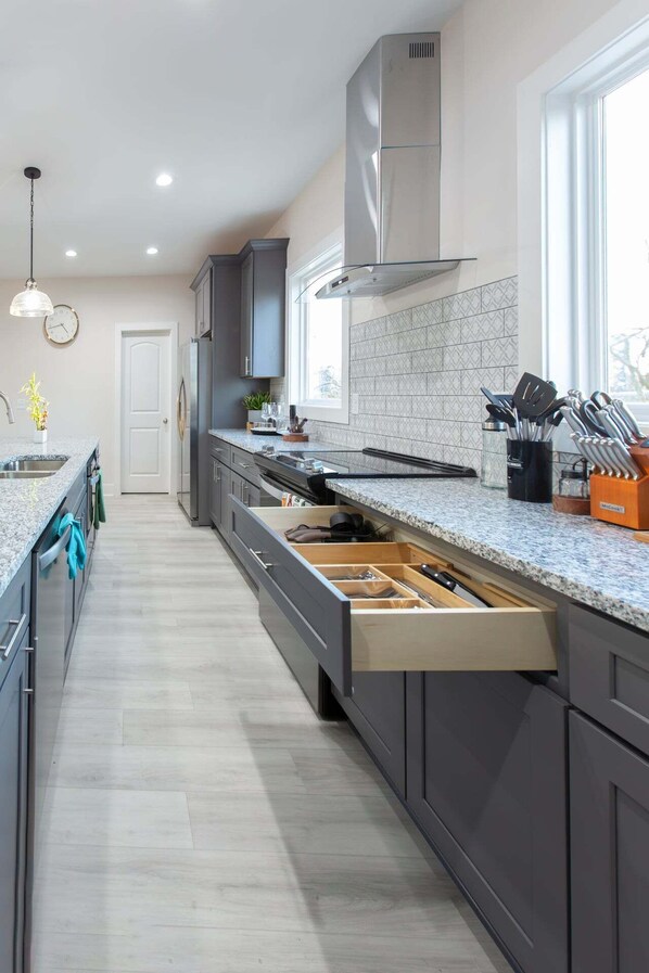 A modern kitchen with grey cabinets, a stainless steel range hood, and a large window providing natural light. - ★HOT AREA★ 5min to Broadway • SLEEPS 12 • SPACIOUS  (Nashville)