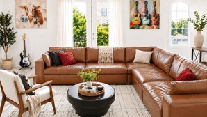 A living room with a brown leather sectional sofa, a round coffee table, a guitar, and artwork on the walls. - ★HOT AREA★ 5min to Broadway • SLEEPS 12 • SPACIOUS  (Nashville)