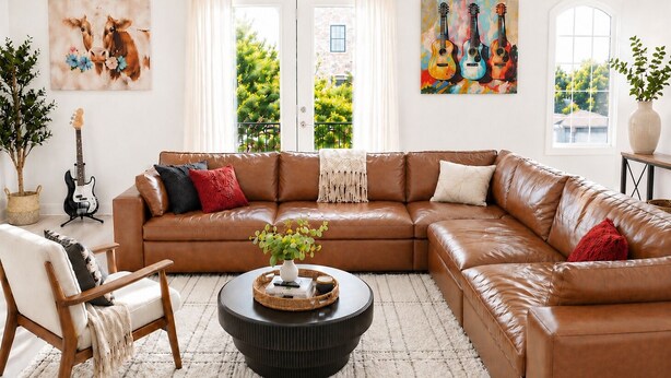 A living room with a brown leather sectional sofa, a round coffee table, a guitar, and artwork on the walls. - ★HOT AREA★ 5min to Broadway • SLEEPS 12 • SPACIOUS  (Nashville)