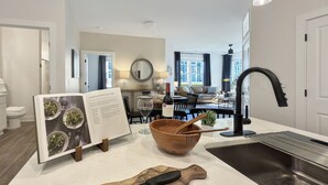 A modern kitchen with a wooden cutting board, a large wooden bowl, and a wine bottle. - Modern Comfort Near Mooresville's Attractions (Mooresville)