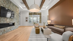 A modern living room with a stone wall, wooden floor, a flat-screen TV, a sofa, a coffee table, and a hanging light fixture. - Modern Comfort Near Mooresville's Attractions (Mooresville)