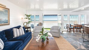 A spacious living room with a view of the beach, furnished with a blue sofa, striped armchairs, and a coffee table. - Luxury Oceanfront Condo - Perfect for Large Families - Steps to the Sand! (Newport Beach)