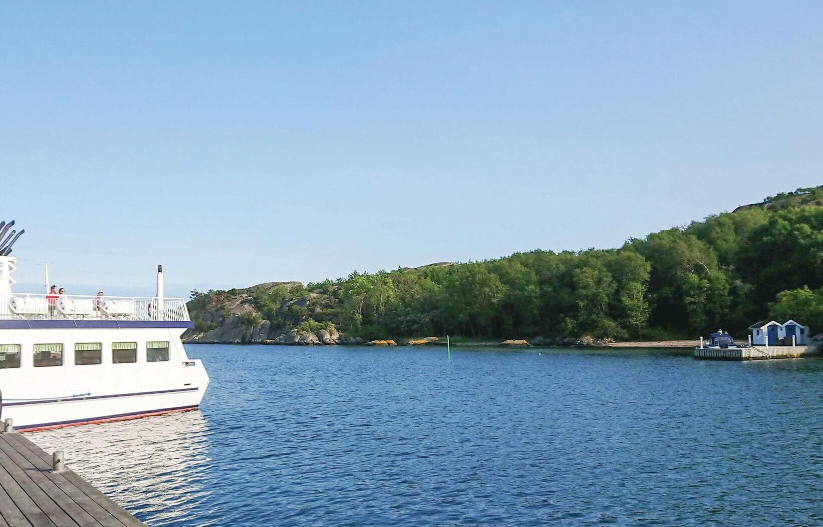 A boat docked at a pier with a forested hillside in the background.