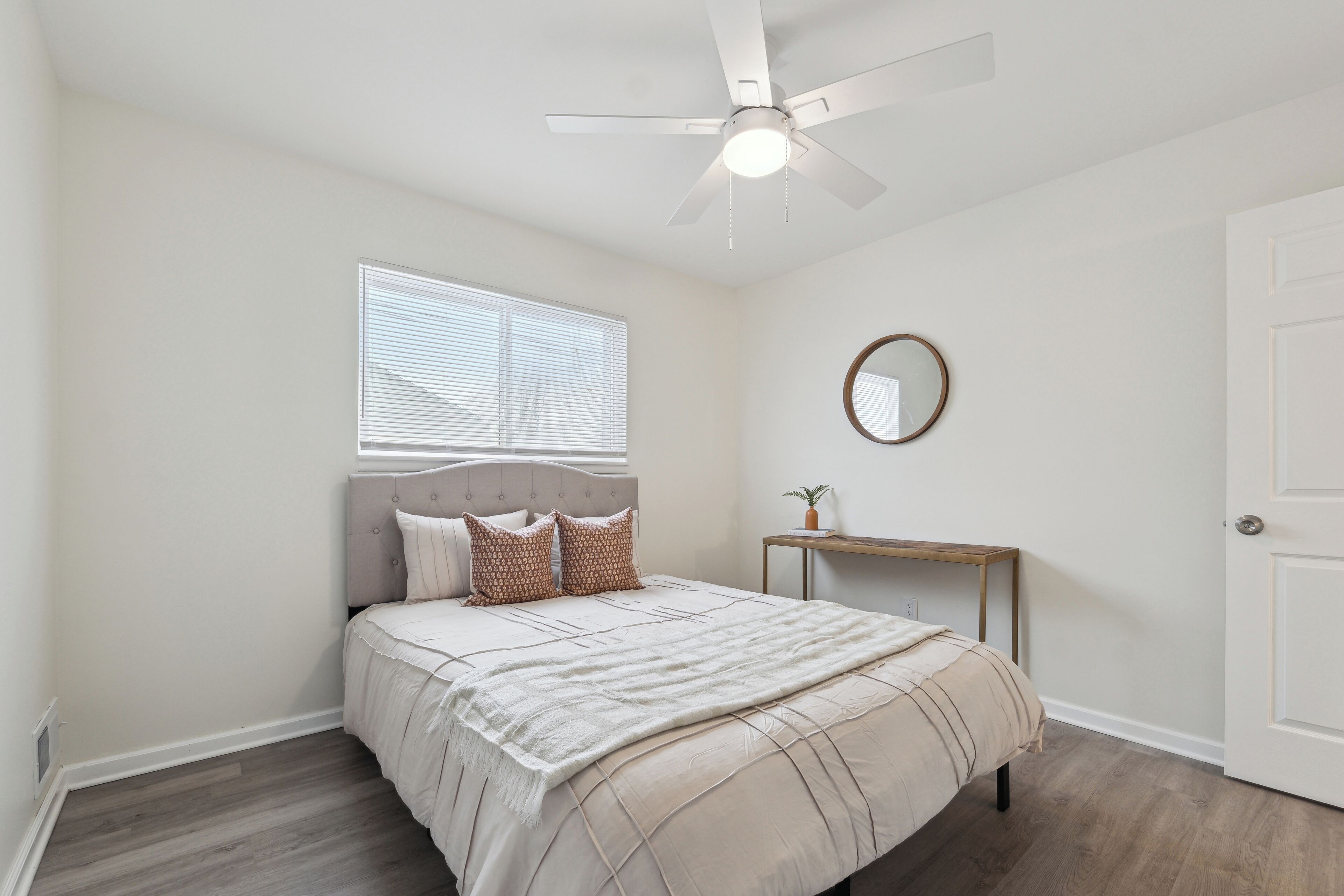 A bedroom with a bed, a ceiling fan, a window, a bedside table, and a door.