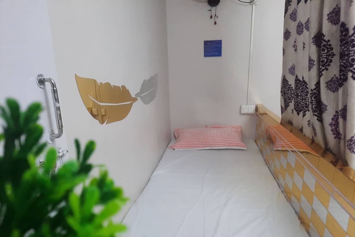 A small, single-bed room with a white mattress, a red and white striped pillow, a wall-mounted towel rack, and a decorative wall piece.