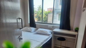 A small, clean room with a bed, a desk, and a window overlooking a building.