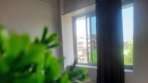 A room with a large window, a white curtain, and a view of buildings outside.