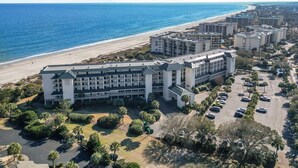 Un hotel frente al mar con varias edificaciones, un estacionamiento y una playa al fondo.