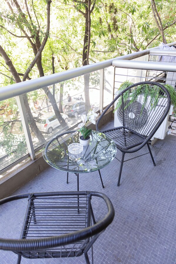 Enjoy the street view from this balcony with a potted plant and two comfortable chairs.