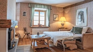 Ein gemütliches Zimmer mit Bett, Sessel, Tisch und Lampe.