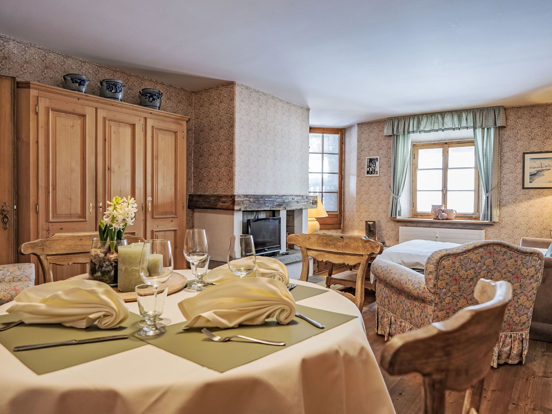 A dining area with a table set for two, wooden cabinets, a fireplace, and a window with curtains.