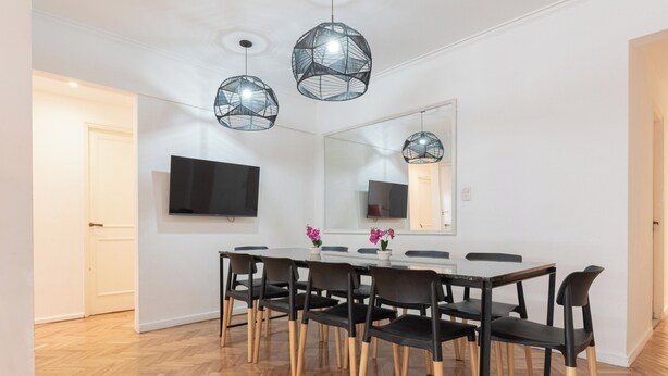 A dining area with a long table, black chairs with wooden legs, and three black pendant lights. - MOT Charcas 3000 (Buenos Aires)