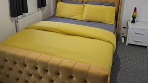 A bed with a tufted headboard, a bedside table with drawers, and a radiator. - West Winds Sleeps 4 with Garden (Wolverhampton)
