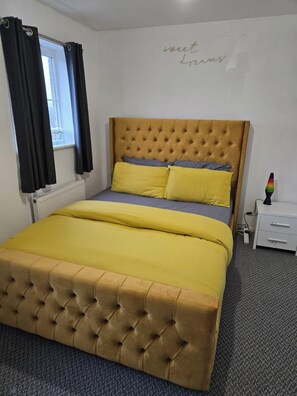 A bed with a tufted headboard, a bedside table with drawers, and a radiator. - West Winds Sleeps 4 with Garden (Wolverhampton)