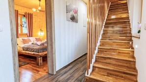 Un escalier en bois mène à une chambre à coucher qui contient un lit, une table de chevet et un luminaire fixé au mur.