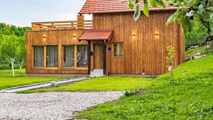 Une maison moderne en bois, avec un toit rouge, de grandes fenêtres et une allée gravillonnée.