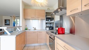 A modern kitchen with wooden cabinets, stainless steel appliances, and a red pot on the counter. - Vacation home Laura by Interhome (Gassin)