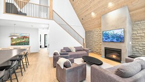 En rummelig opholdsstue med pejs, et tv monteret på en stenvæg og en trappe til en etage ovenover.