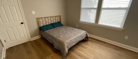 A bedroom with a bed, a door, and two windows.