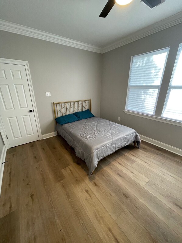 Une chambre à coucher avec un lit, un ventilateur de plafond, une fenêtre et une porte.