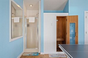 A room with a shower, a door leading to a bathroom, and a ping pong table.