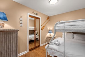 A room with bunk beds, a wicker side table, a nightstand with a lamp, and a door leading to another room.