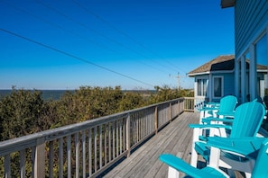 A wooden deck with chairs, overlooking a beach and ocean.