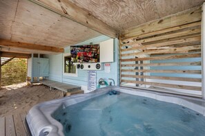 A hot tub area with a wooden ceiling, a wall-mounted TV, and a wooden fence.
