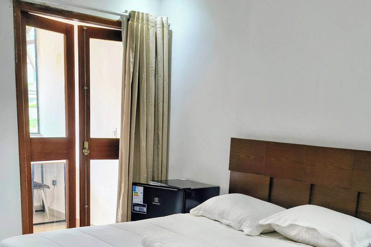 A hotel room with a bed, a nightstand, a wooden headboard, a window with curtains, and an air conditioning unit.