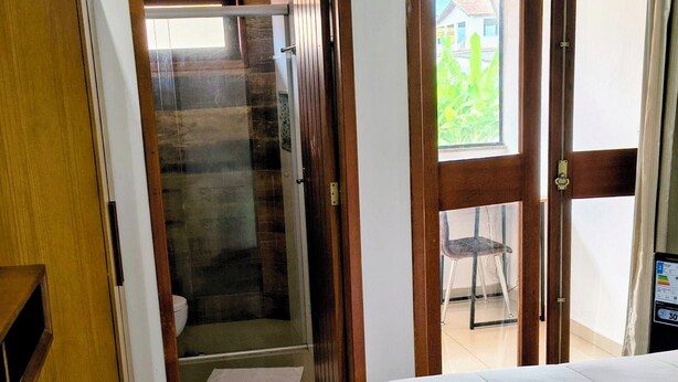 Une chambre d’hôtel avec un lit, une armoire en bois, un espace douche et une vue sur l’extérieur grâce à une porte vitrée.