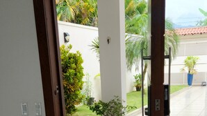 Un couloir avec une porte en bois donnant sur un patio agrémenté de plantes en pot et offrant une vue sur l’extérieur.