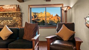 A cozy living room with a stone fireplace, a large window with a view of rocky terrain, and two leather armchairs with cushions. - Walk to Uptown + Hot Tub, Firepit, Epic Views (Sedona)