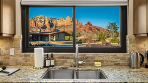 A kitchen with a granite countertop, stainless steel sink, and a window overlooking a mountainous landscape. - Walk to Uptown + Hot Tub, Firepit, Epic Views (Sedona)