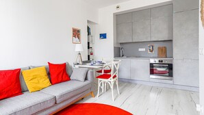 A modern apartment with a grey sofa, red and yellow cushions, a white dining table, and a kitchen with grey cabinets and a built-in oven. - Le Palais du Vieux Port by Interhome (Nice)