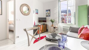 A modern living room with a dining area, a TV, and a view of a cityscape through large windows. - Le Palais du Vieux Port by Interhome (Nice)
