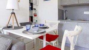 A compact kitchen with white cabinets, a sink, and a dining area with a white table and chairs. - Le Palais du Vieux Port by Interhome (Nice)