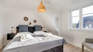 A bedroom with a bed, bedside tables, a hanging light fixture, a dreamcatcher, and a window with a view of a house. - Thilo - "Charming vacation home on Sylt: relaxation and recreation await you!" (Sylt / OT Tinnum)