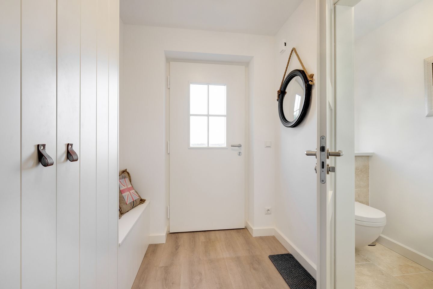 Un couloir avec une porte blanche, une petite fenêtre et un miroir accroché au mur.