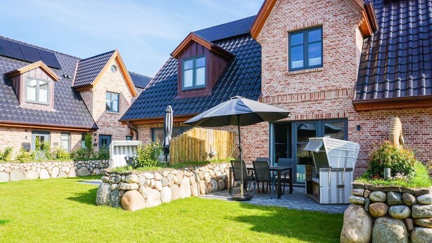 A residential property with a brick exterior, a stone retaining wall, a grassy lawn, and outdoor furniture. - Thilo - "Charming vacation home on Sylt: relaxation and recreation await you!" (Sylt / OT Tinnum)