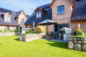 Um imóvel residencial com fachada de tijolos, muro de arrimo em pedra, gramado e mobiliário de exterior.