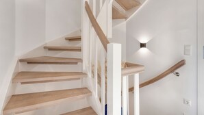 A modern staircase with wooden steps and white railings, leading to a landing with a wall-mounted light fixture. - Thilo - "Charming vacation home on Sylt: relaxation and recreation await you!" (Sylt / OT Tinnum)