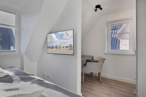 A bedroom with a bed, a desk, and a chair, a window with a view of a building, and a ceiling light. - Lena - "Your perfect vacation paradise on Sylt - the vacation home Lena awaits you (Sylt / OT Tinnum)