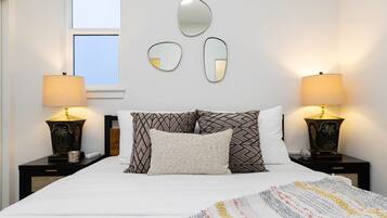 A neatly made bed with patterned pillows, two bedside lamps, and three wall mirrors.
