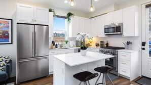 Uma cozinha moderna com armários brancos, eletrodomésticos de aço inoxidável, uma ilha central com banquetas e iluminação pendente.