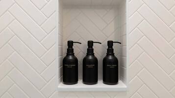 Ein weißes Regal mit drei schwarzen Flaschen, beschriftet mit Conditioner, Shampoo und Duschgel.