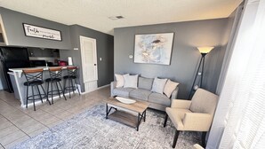 Un salon moderne avec un canapé gris, une table basse et un coin bar équipé de tabourets.