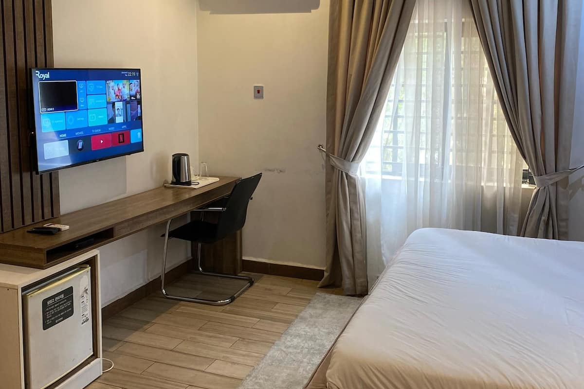 Una habitación de hotel moderna con una cama, un escritorio con una silla, un televisor y un equipo de aire acondicionado.