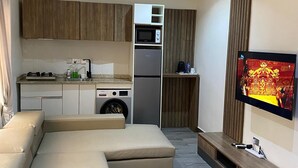 Een moderne woonkamer met een modulaire bank, een flatscreen televisie aan de muur en een keuken met een magnetron en koelkast.