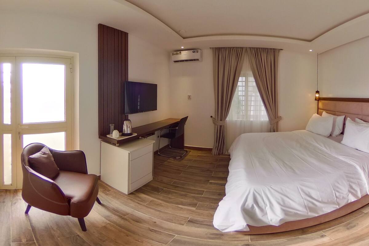 Una habitación de hotel con una cama grande, un escritorio con una silla, un televisor y un teléfono en una mesita de noche.